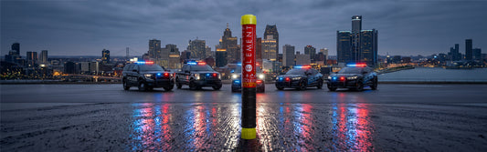An Element fire extinguisher positioned in front of police vehicles and a city skyline at night.   