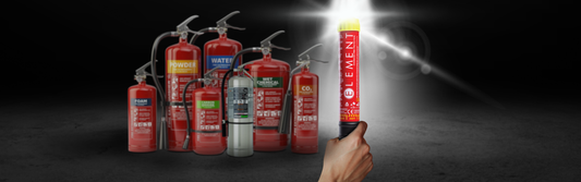 Hand holding an Element fire extinguisher with a bright light emitting from the tip, contrasted against a lineup of traditional pressurized fire extinguishers (foam, water, powder, CO₂) in the background.