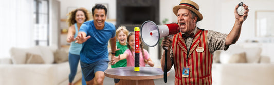 A carnival barker announces through a megaphone as a smiling family races toward an Element fire extinguisher displayed on a table.