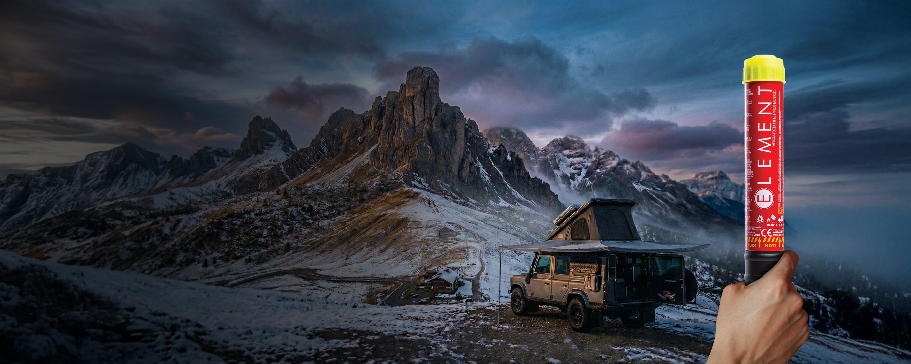 Element Fire Extinguisher held in front of a fully equipped overlanding vehicle parked in front of a scenic winter mountain landscape.